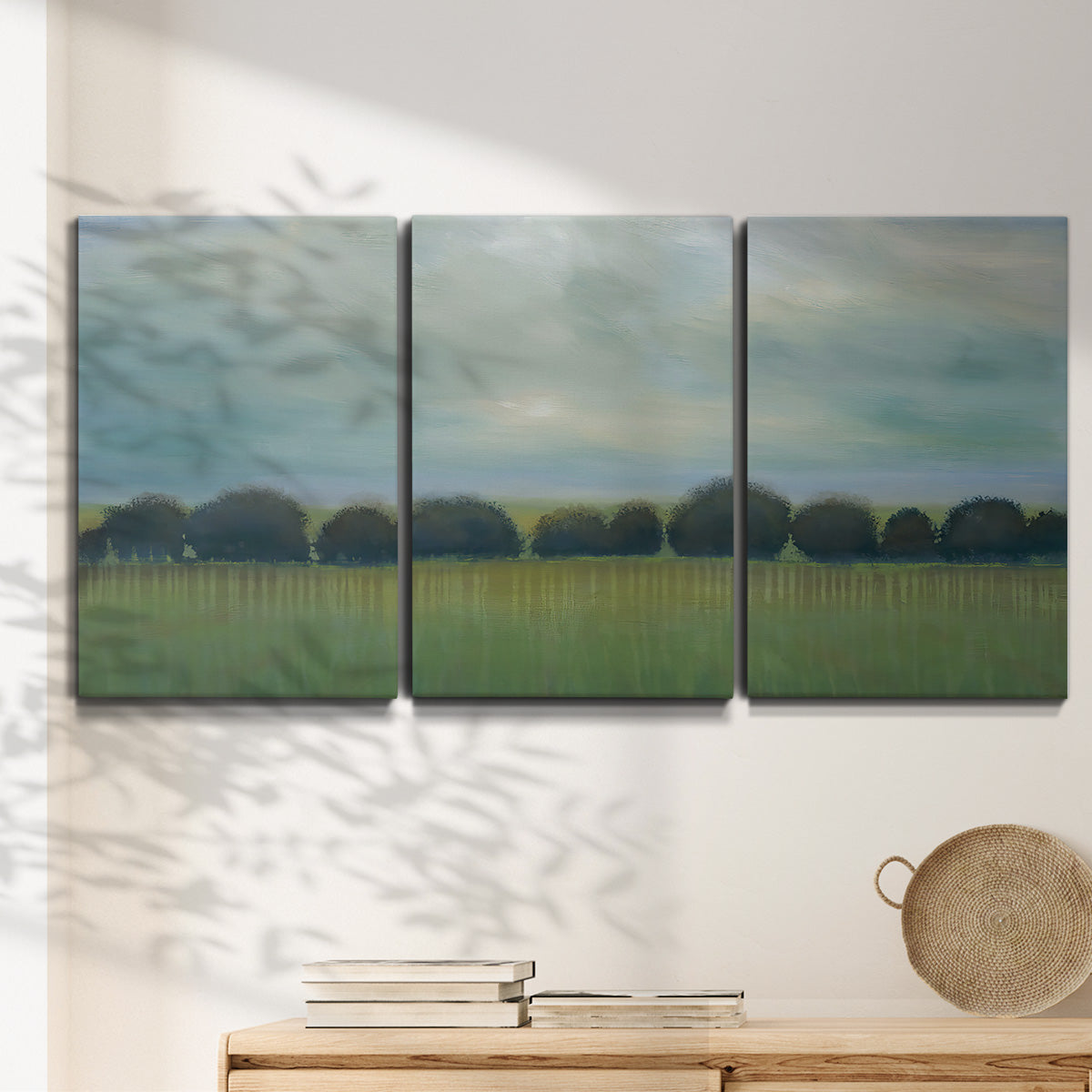 Three-panel canvas wall art featuring rolling green pastoral fields, displayed in a minimalist living room above a console table.