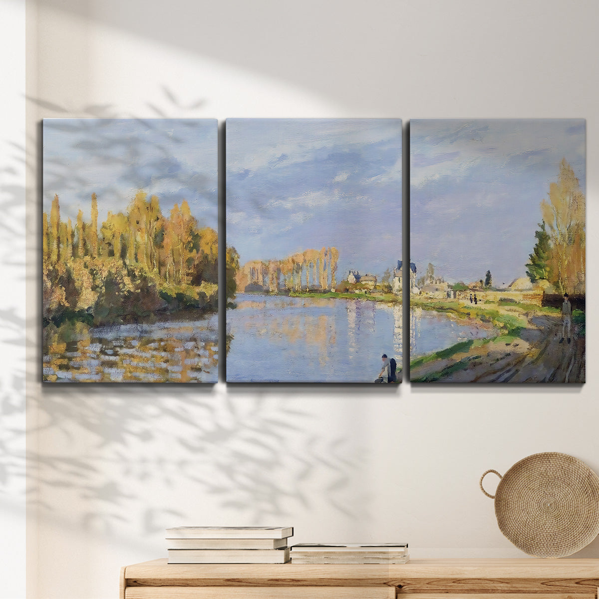 Three-panel canvas wall art featuring river flowing past village, displayed in a minimalist living room above a console table.
