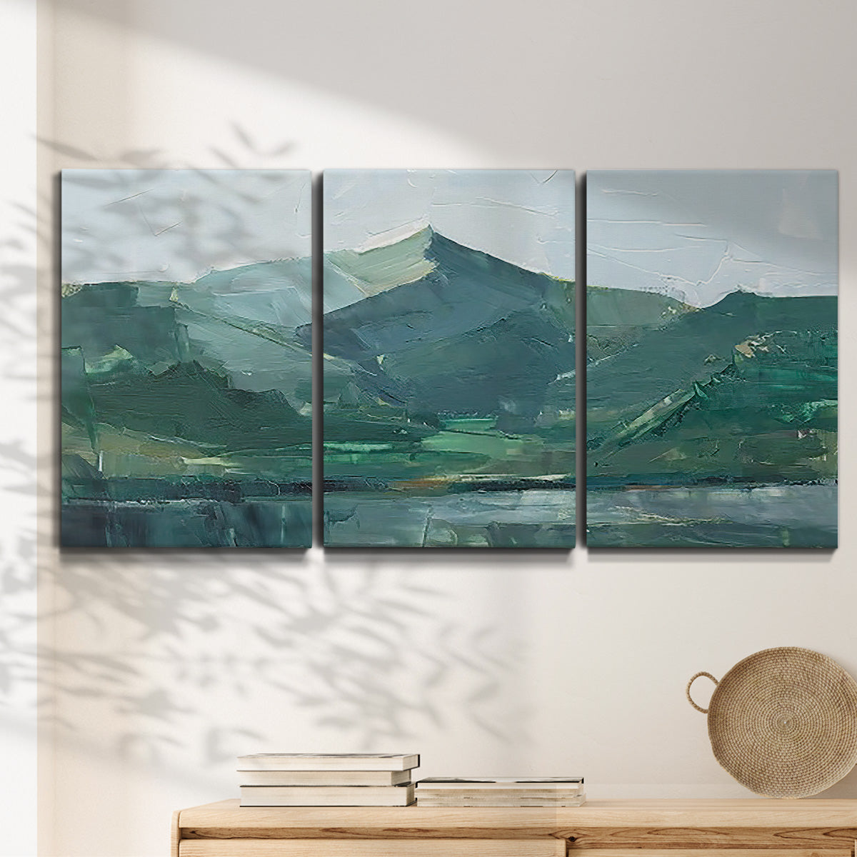 Three-panel canvas wall art featuring muted mountain range in grey tones, displayed in a minimalist living room above a console table.