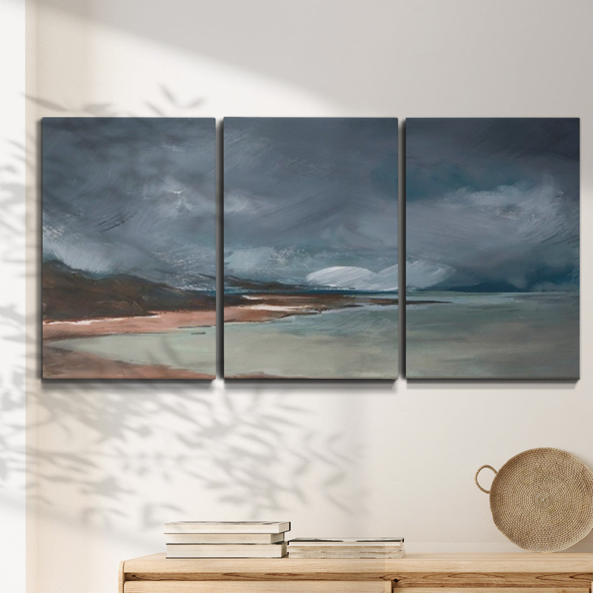 Three-panel canvas wall art featuring stormy sea glass toned coastline, displayed in a minimalist living room above a console table.
