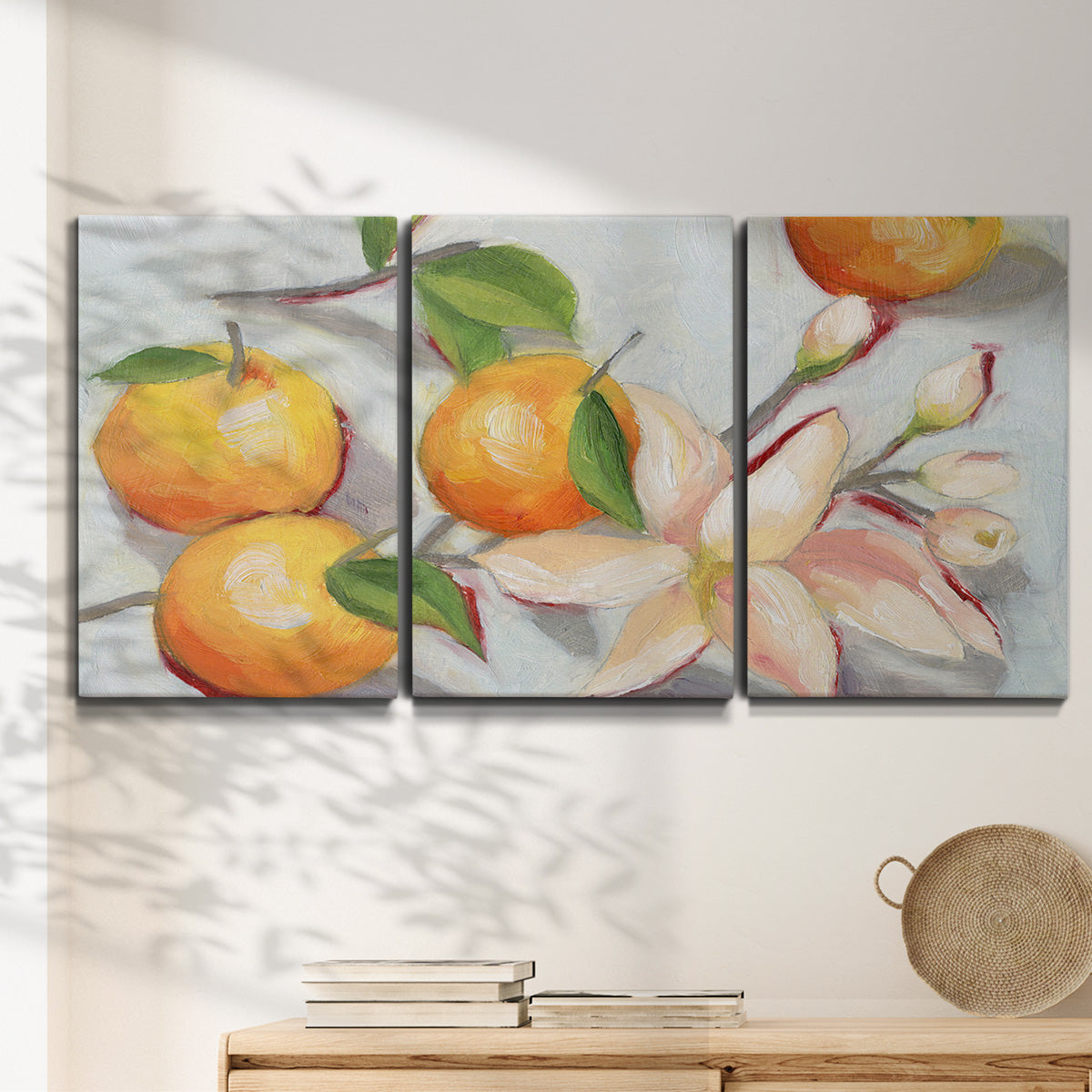 Three-panel canvas wall art featuring bright tangerine still life blossoms, displayed in a minimalist living room above a console table.