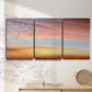 Three-panel canvas wall art featuring glowing sunset sky over landscape, displayed in a minimalist living room above a console table.