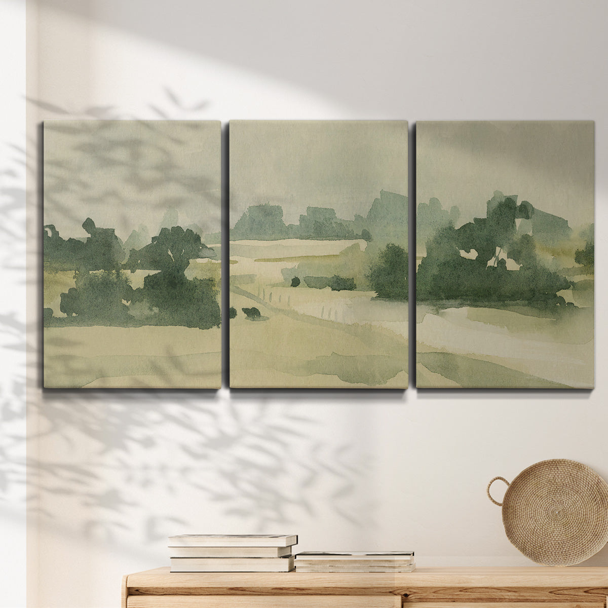 Three-panel canvas wall art featuring pasture landscape in soft watercolor, displayed in a minimalist living room above a console table.