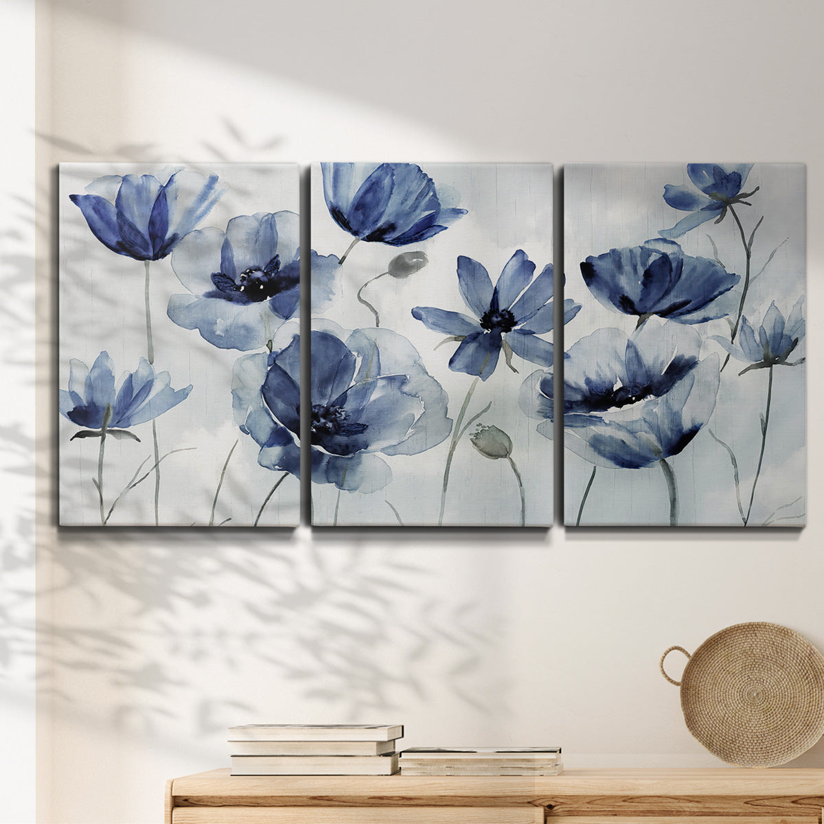 Three-panel canvas wall art featuring indigo floral blossoms awakening, displayed in a minimalist living room above a console table.