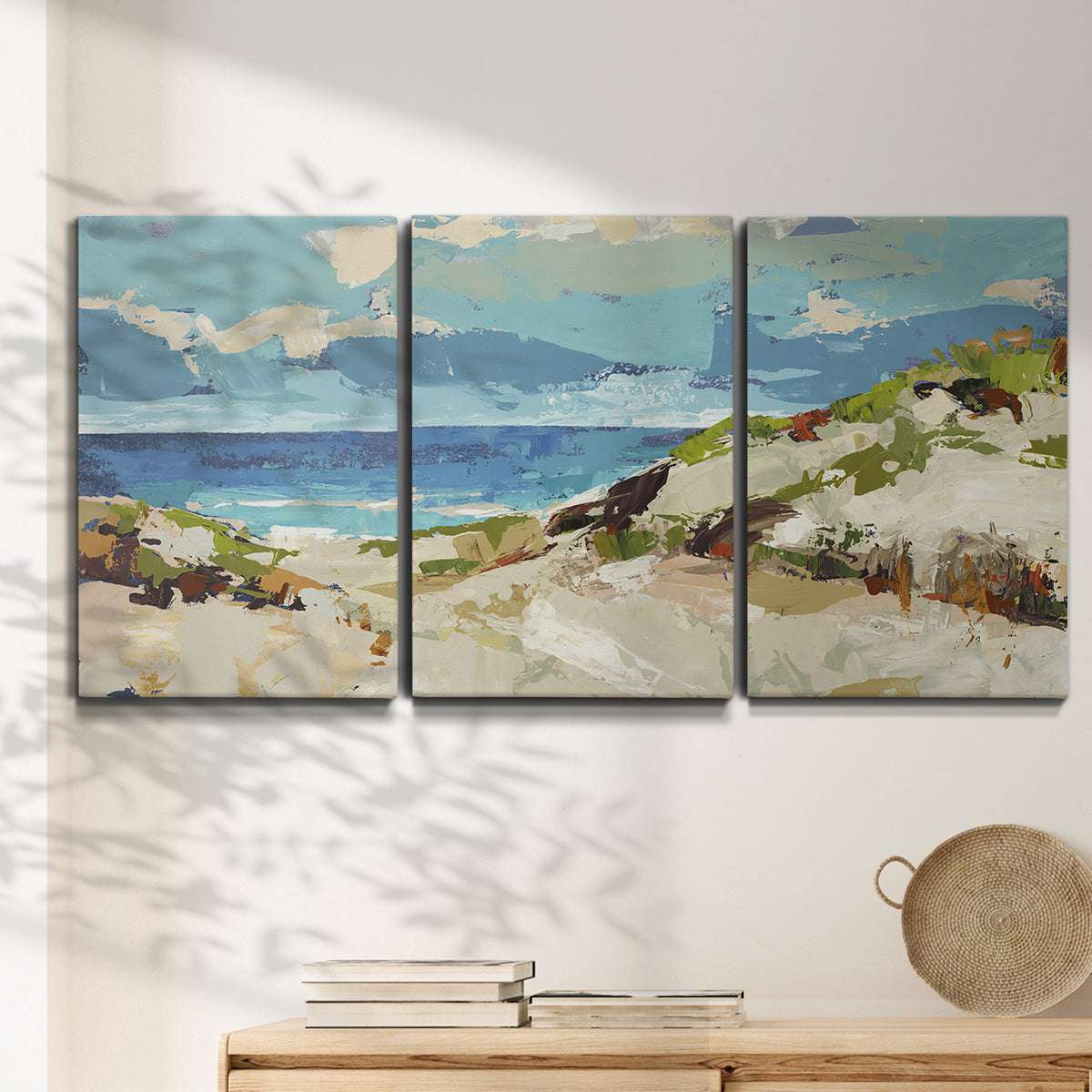 Three-panel canvas wall art featuring sand dunes beside open water, displayed in a minimalist living room above a console table.