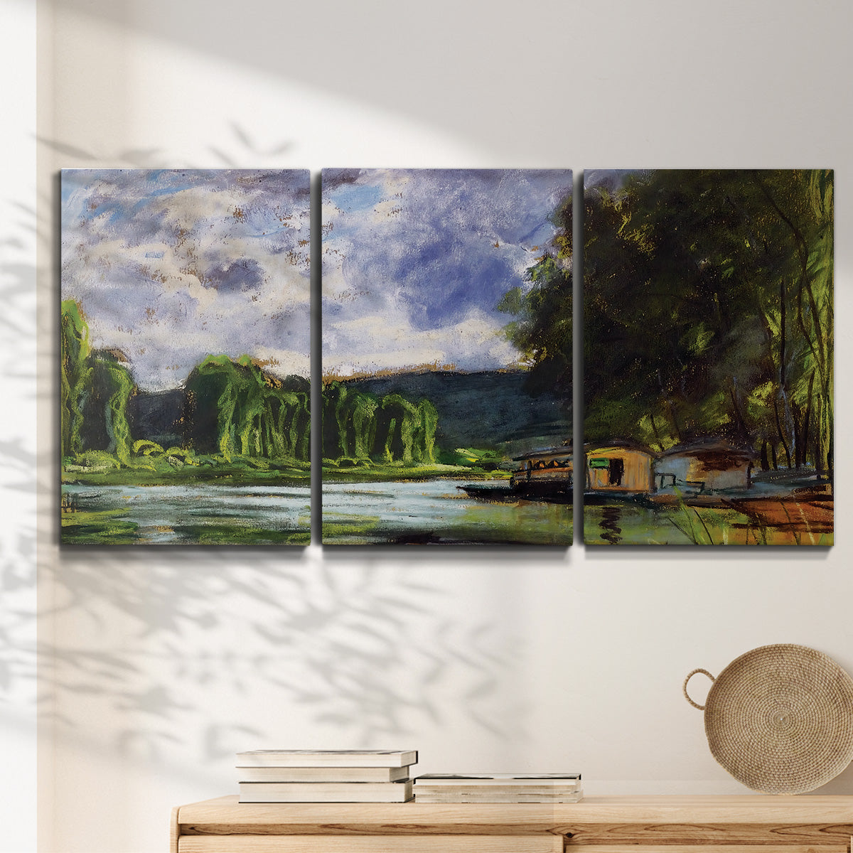 Three-panel canvas wall art featuring riverbank landscape near village, displayed in a minimalist living room above a console table.