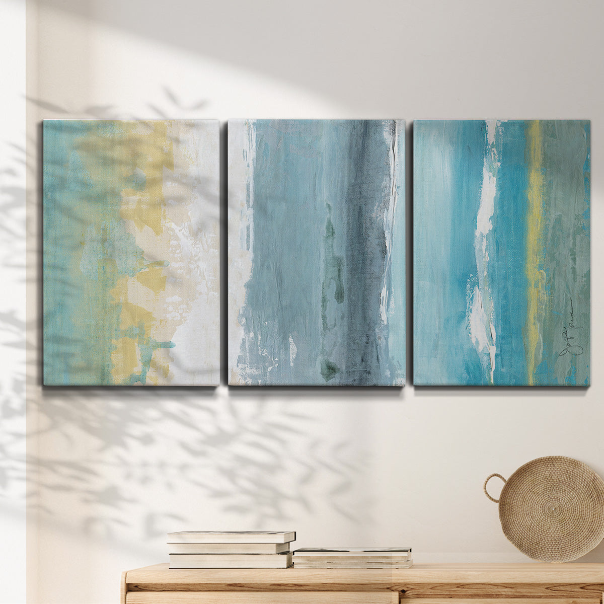 Three-panel canvas wall art featuring abstract coastal beach textures, displayed in a minimalist living room above a console table.