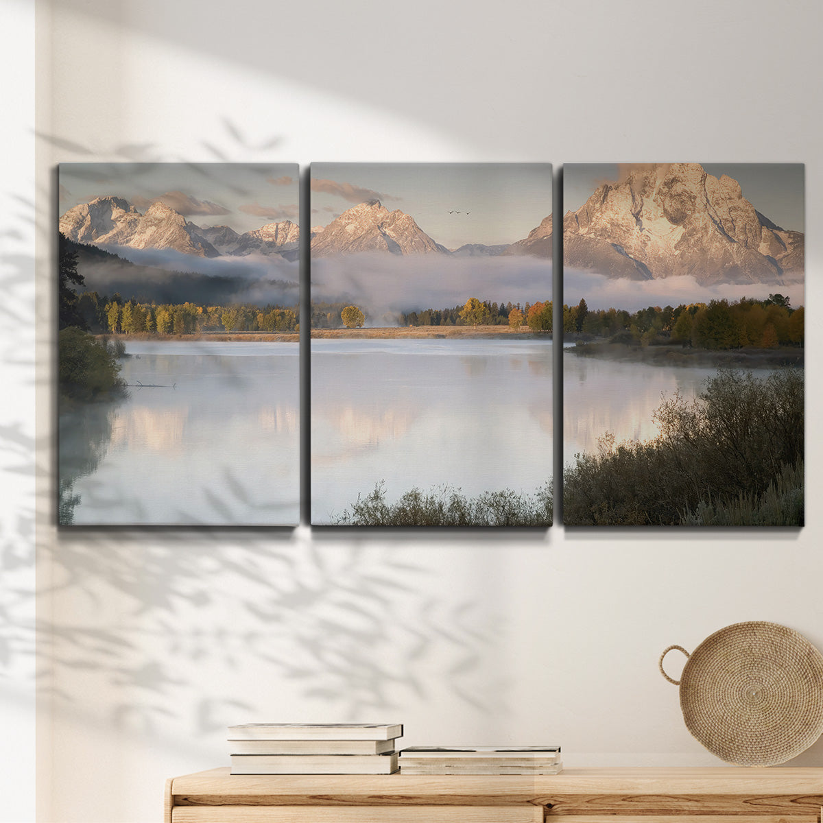Three-panel canvas wall art featuring fog drifting over winding river, displayed in a minimalist living room above a console table.