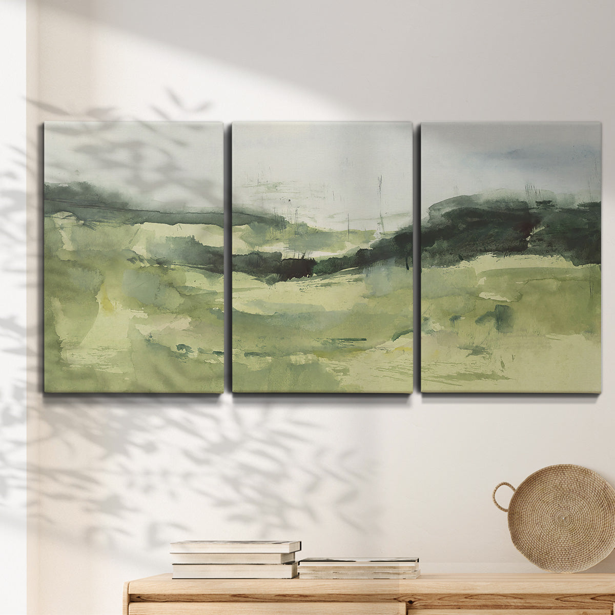 Three-panel canvas wall art featuring rolling hillside countryside landscape, displayed in a minimalist living room above a console table.