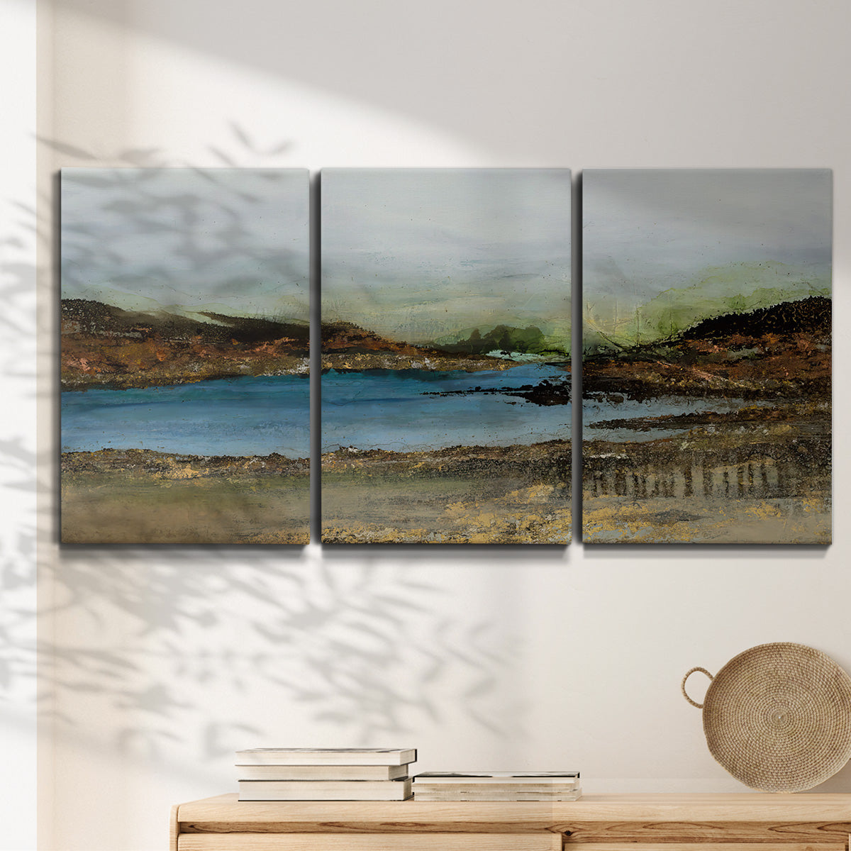 Three-panel canvas wall art featuring peaceful lakeside shoreline landscape, displayed in a minimalist living room above a console table.