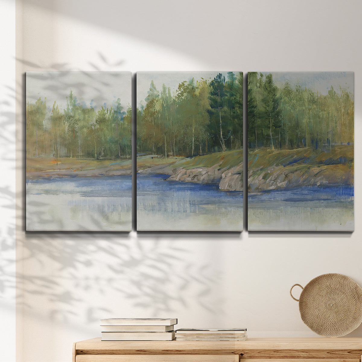 Three-panel canvas wall art featuring riverbank landscape with trees, displayed in a minimalist living room above a console table.