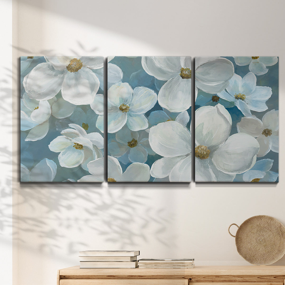 Three-panel canvas wall art featuring soft white floral abstraction, displayed in a minimalist living room above a console table.
