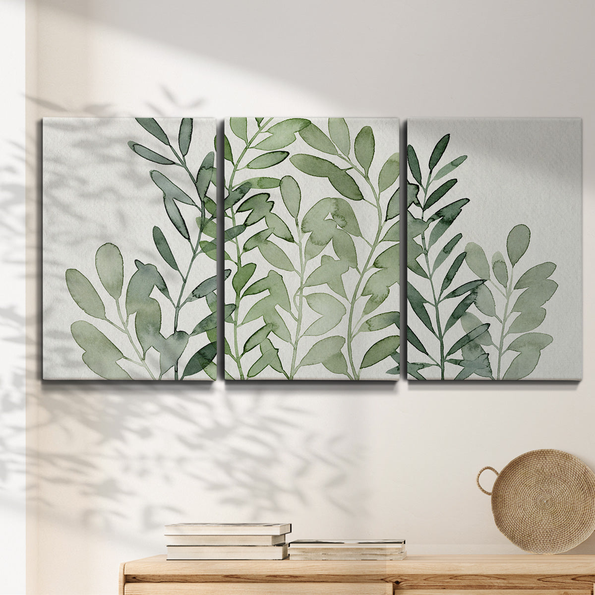 Three-panel canvas wall art featuring foraged leafy greens botanical study, displayed in a minimalist living room above a console table.