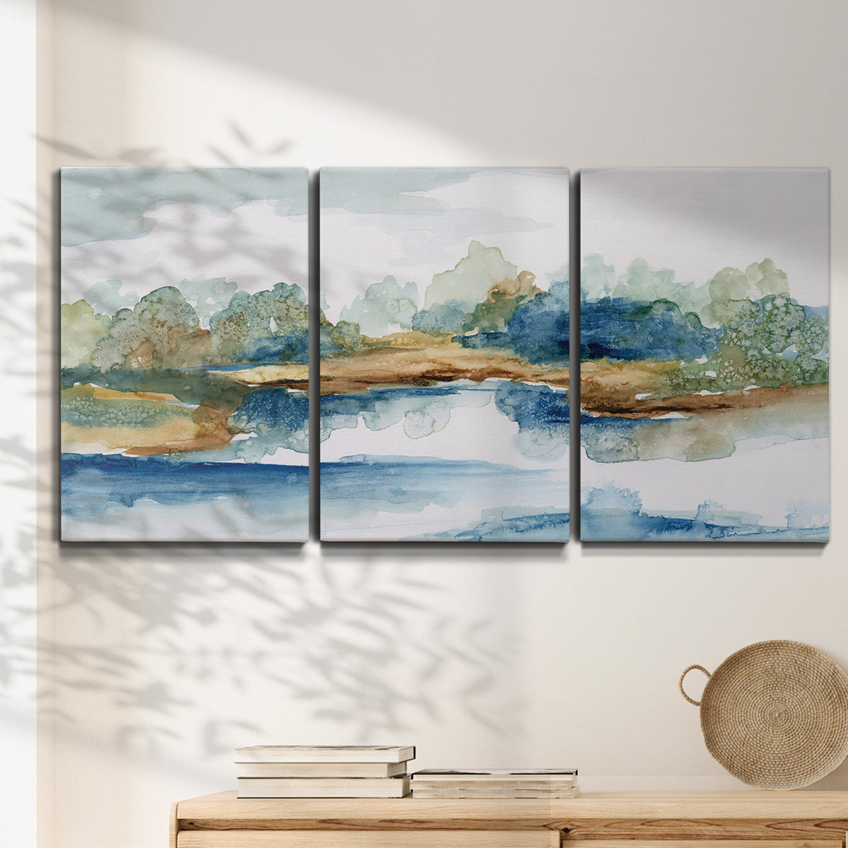 Three-panel canvas wall art featuring abstract blue watercolor landscape, displayed in a minimalist living room above a console table.