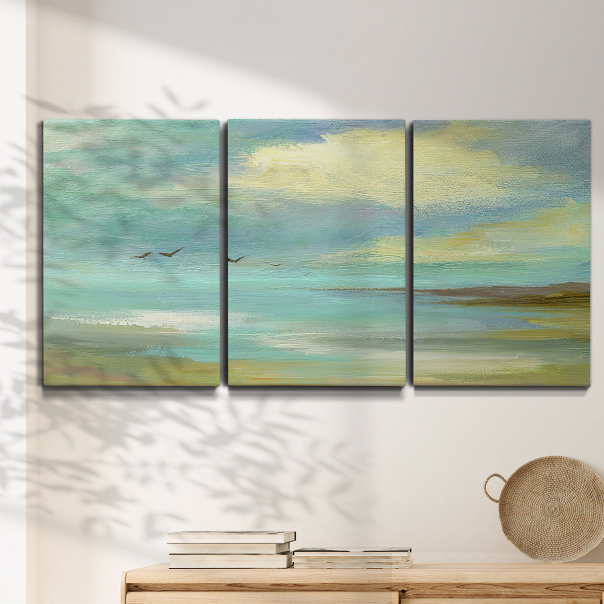 Three-panel canvas wall art featuring calm coastal drift patterns, displayed in a minimalist living room above a console table.