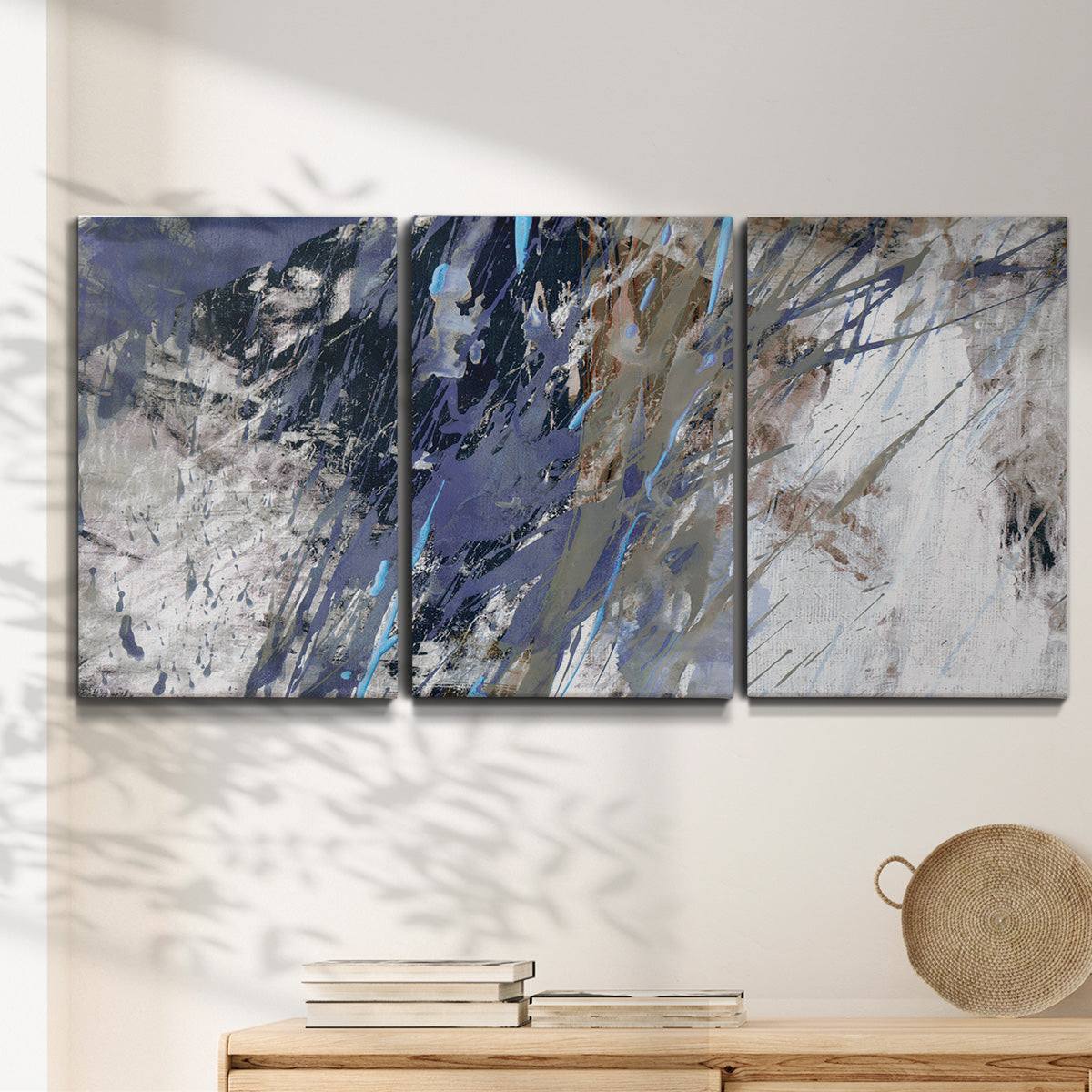 Three-panel canvas wall art featuring textured blue abstract composition, displayed in a minimalist living room above a console table.