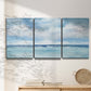 Three-panel canvas wall art featuring tropical clouds over ocean horizon, displayed in a minimalist living room above a console table.