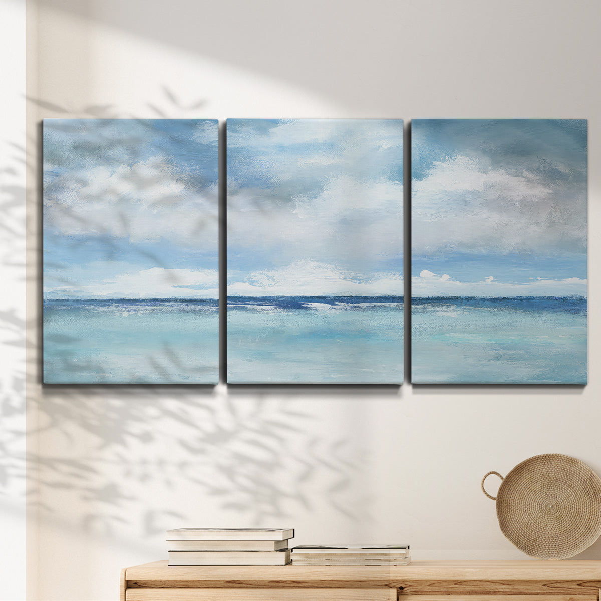 Three-panel canvas wall art featuring tropical clouds over ocean horizon, displayed in a minimalist living room above a console table.