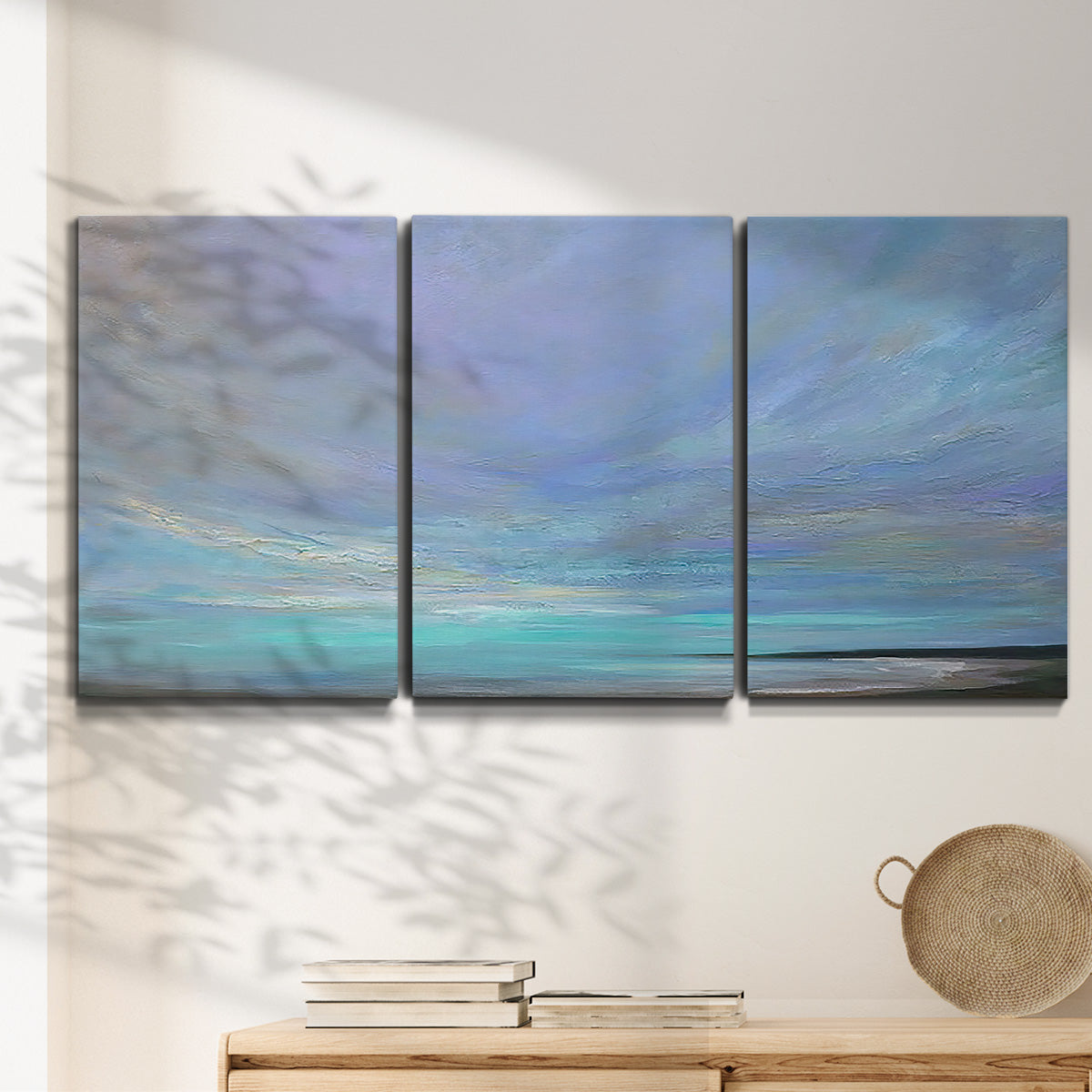 Three-panel canvas wall art featuring coastal shoreline with gentle surf, displayed in a minimalist living room above a console table.