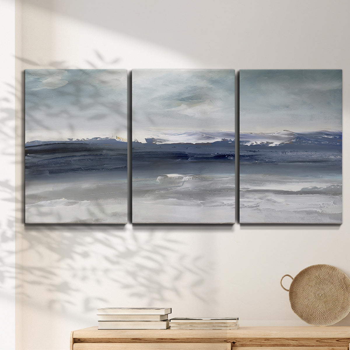 Three-panel canvas wall art featuring abstract coastal tones and movement, displayed in a minimalist living room above a console table.