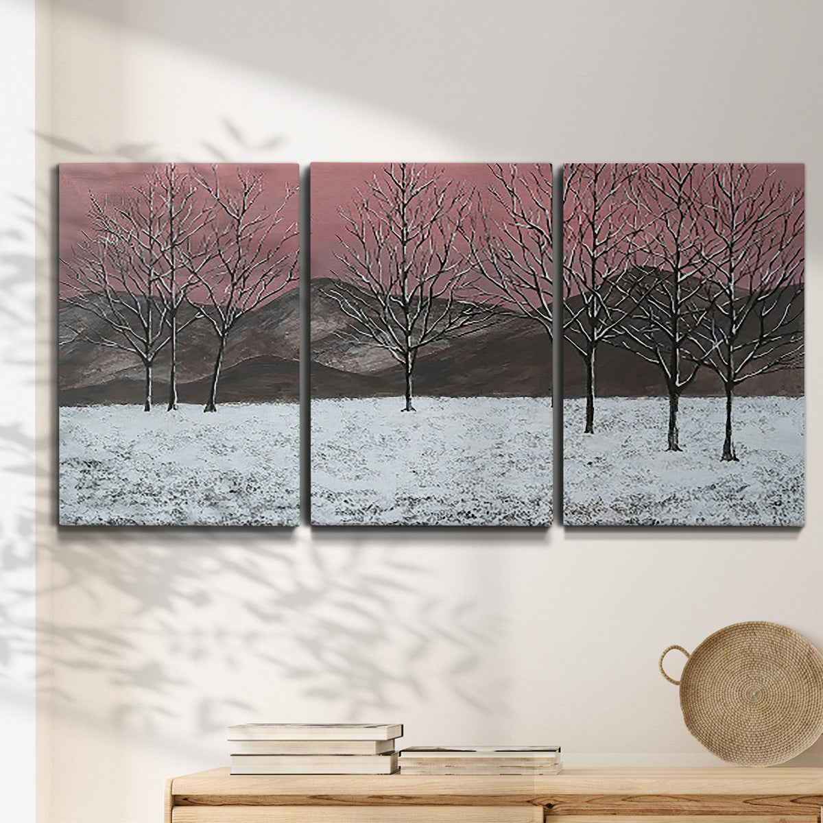 Three-panel canvas wall art featuring winter sunset snowfall landscape, displayed in a minimalist living room above a console table.