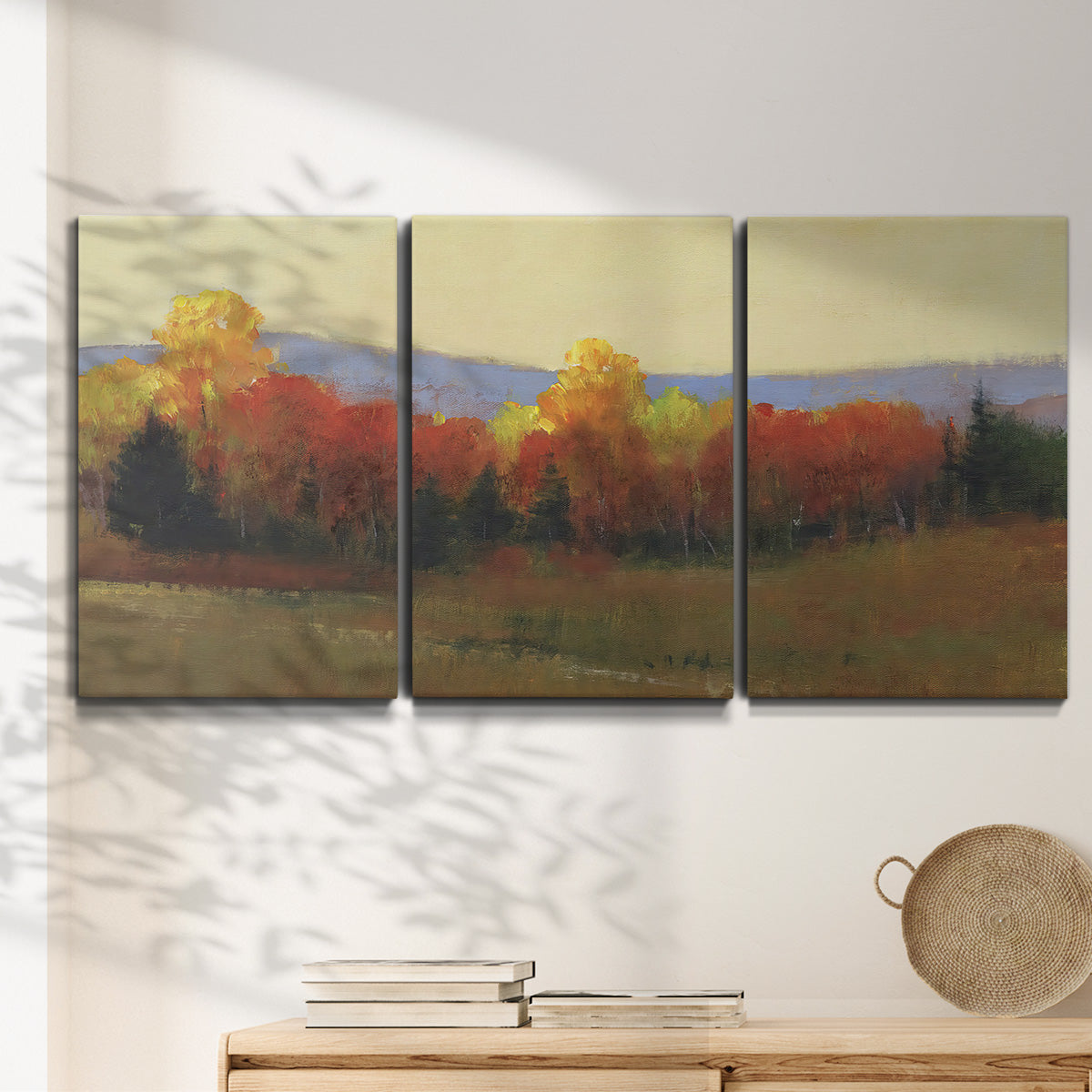Three-panel canvas wall art featuring autumn landscape changing foliage, displayed in a minimalist living room above a console table.