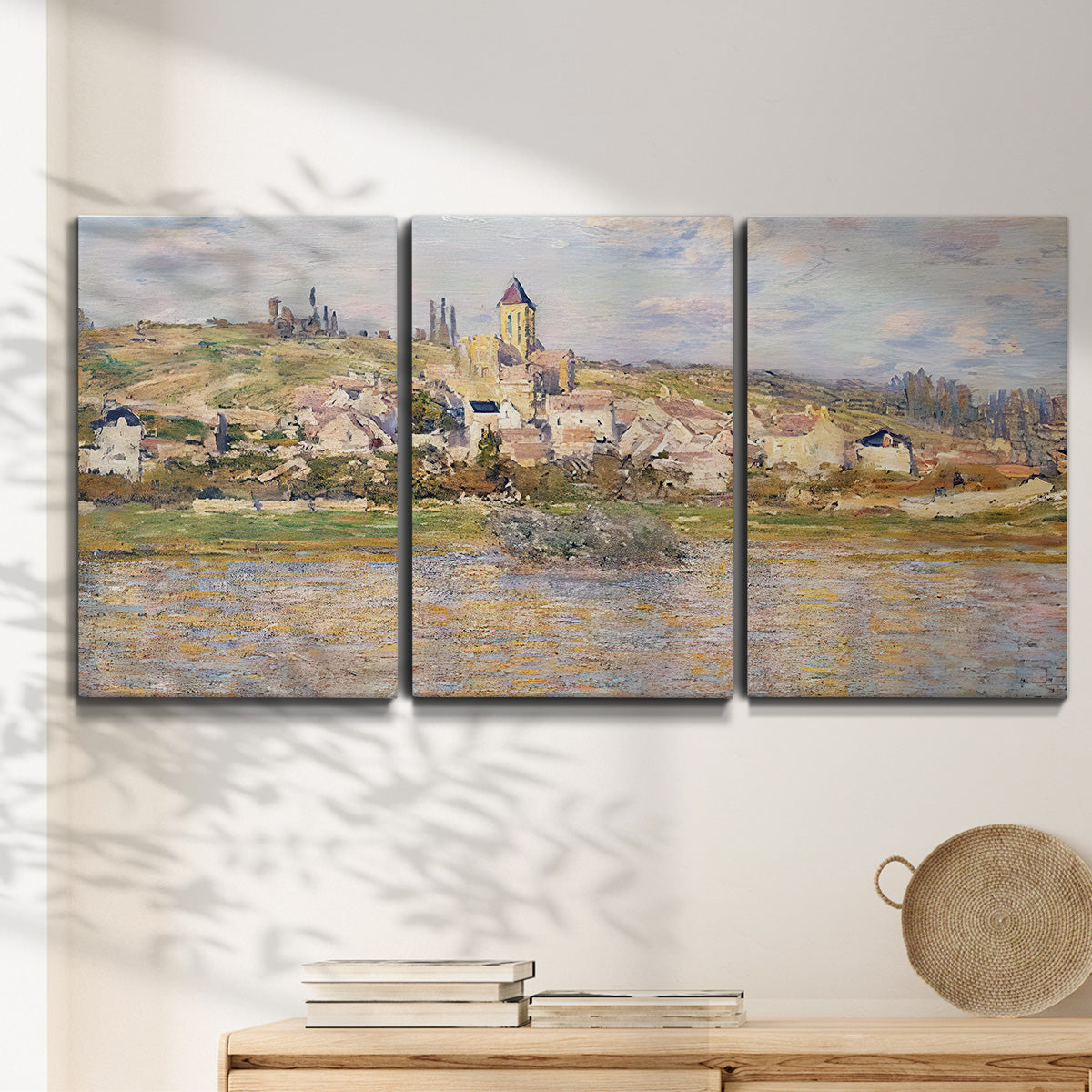 Three-panel canvas wall art featuring village overlooking river valley, displayed in a minimalist living room above a console table.