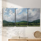 Three-panel canvas wall art featuring pastoral mountain landscape in blue, displayed in a minimalist living room above a console table.