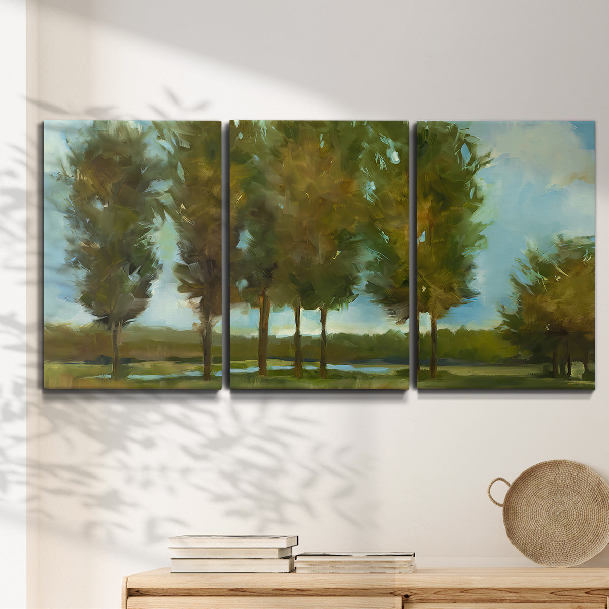 Three-panel canvas wall art featuring tall trees lining open landscape, displayed in a minimalist living room above a console table.