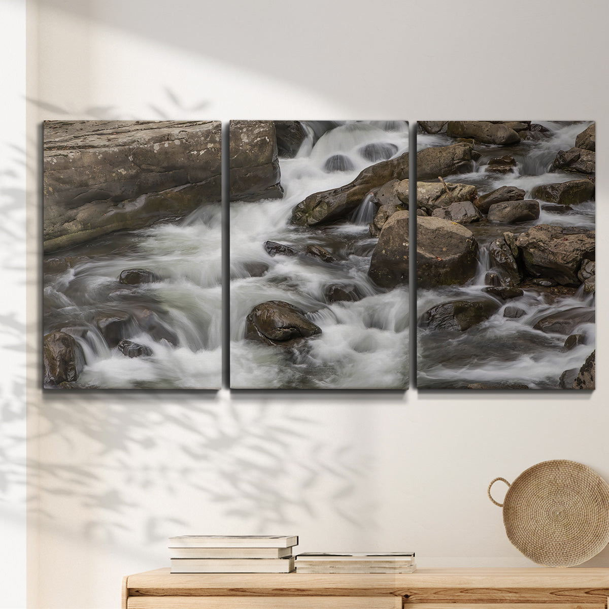 Three-panel canvas wall art featuring rushing river water over rocks, displayed in a minimalist living room above a console table.