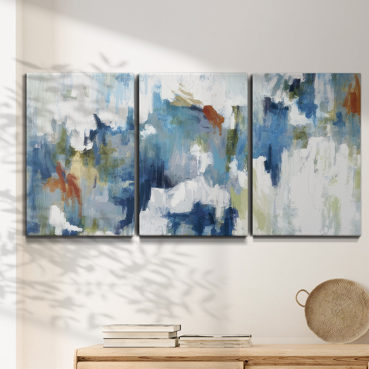 Three-panel canvas wall art featuring flowing abstract color movement, displayed in a minimalist living room above a console table.