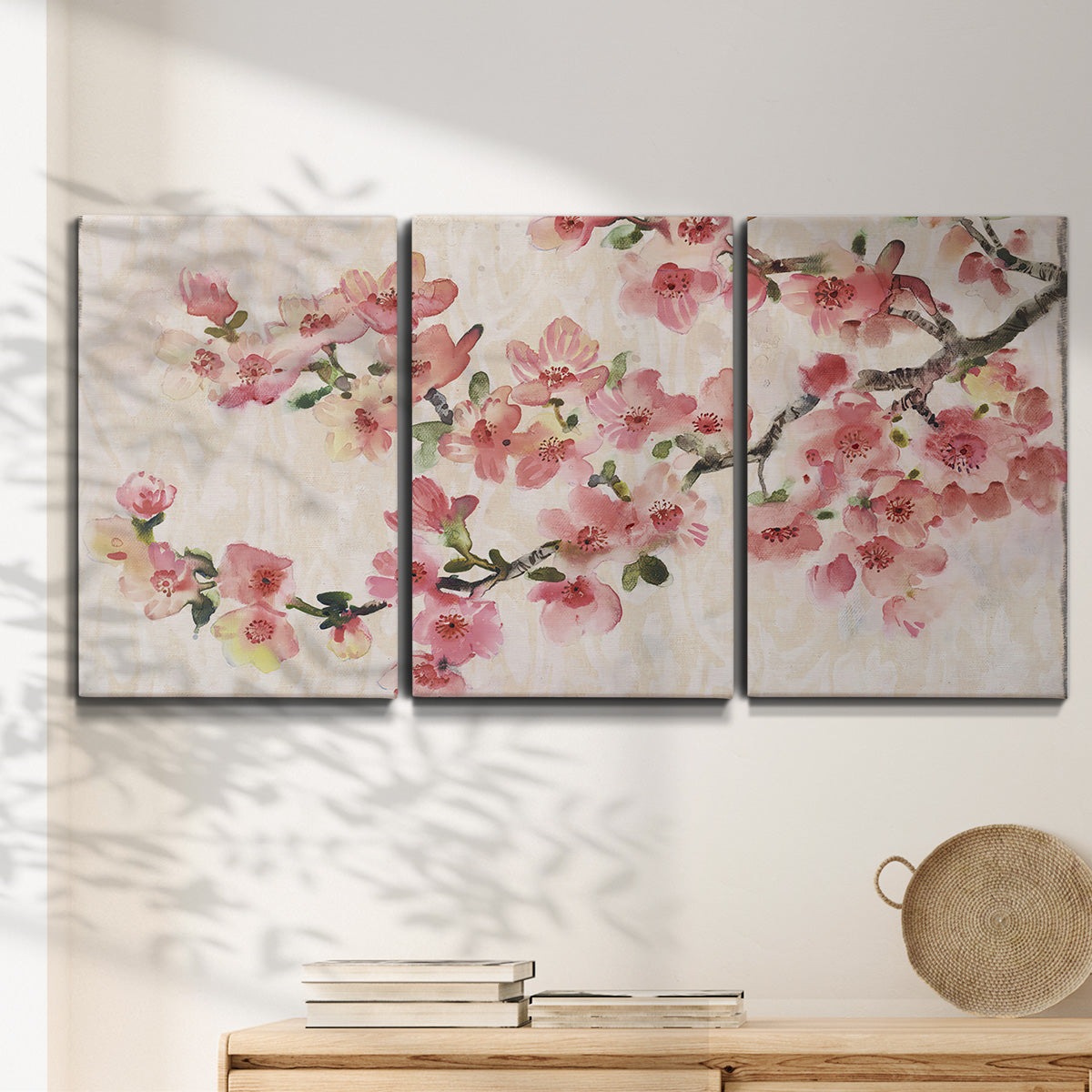 Three-panel canvas wall art featuring blooming cherry blossom branches, displayed in a minimalist living room above a console table.