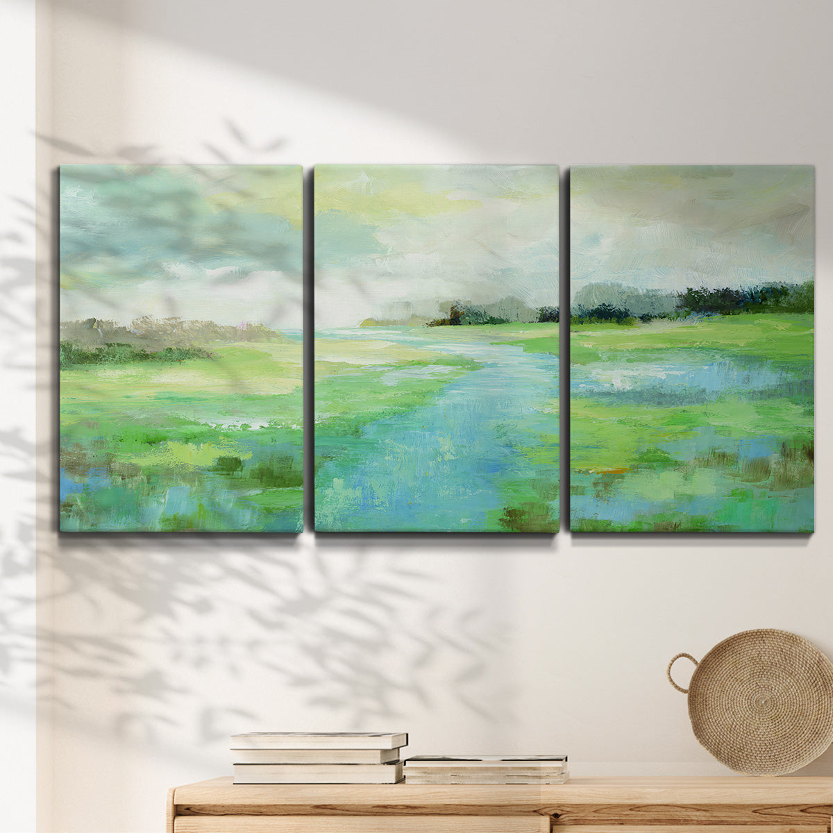 Three-panel canvas wall art featuring gentle stream winding through trees, displayed in a minimalist living room above a console table.