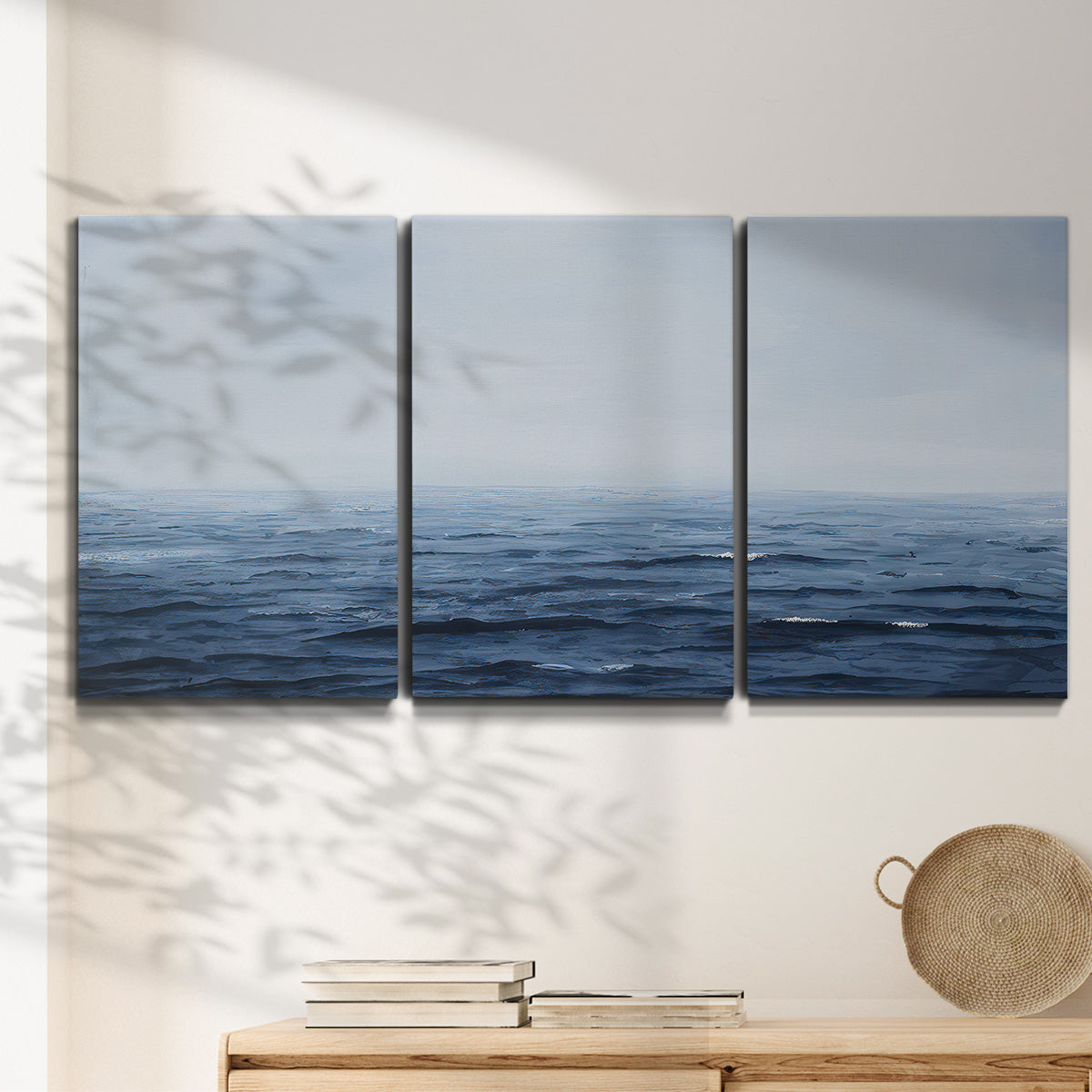 Three-panel canvas wall art featuring grayscale seascape with horizon, displayed in a minimalist living room above a console table.