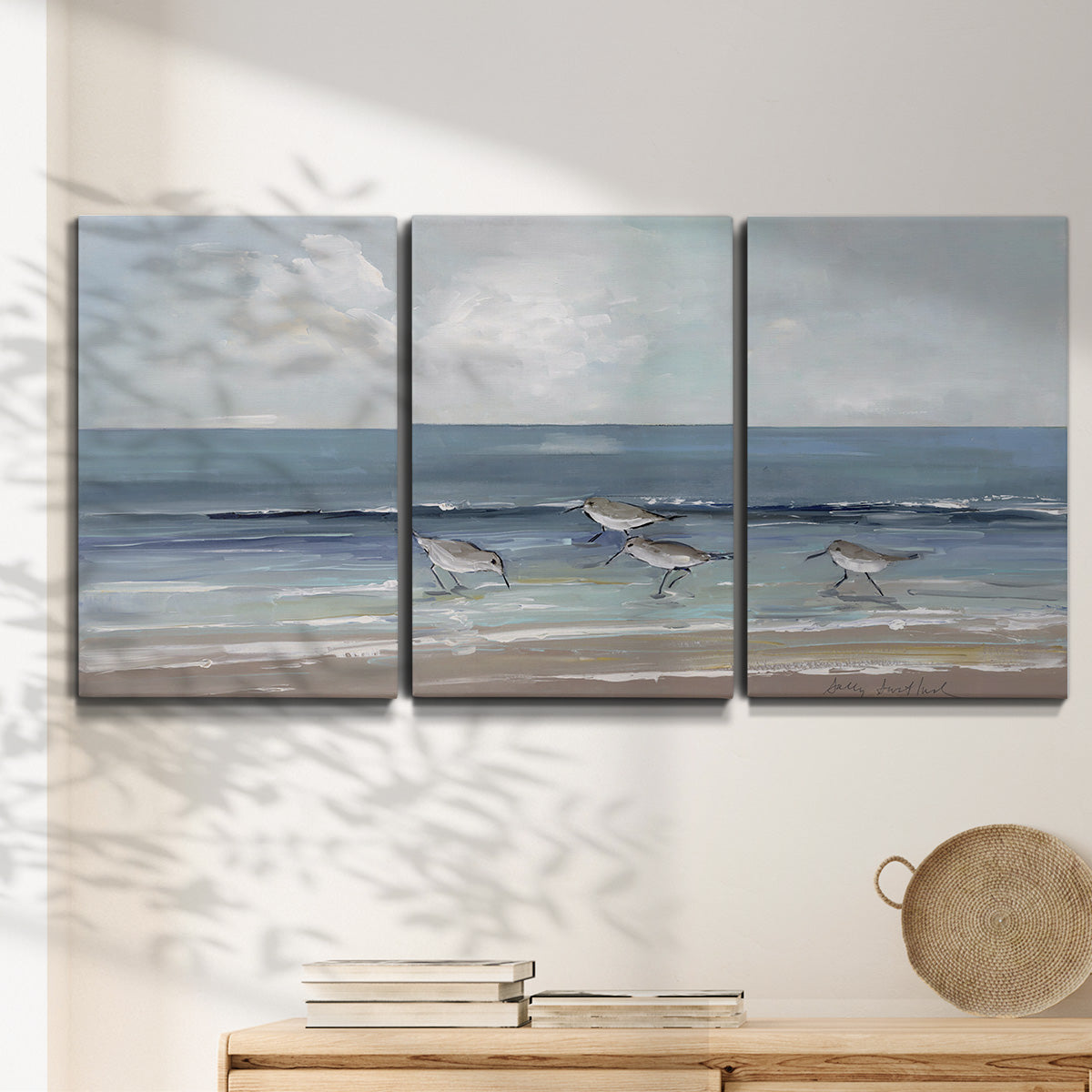 Three-panel canvas wall art featuring shore birds searching along beach, displayed in a minimalist living room above a console table.