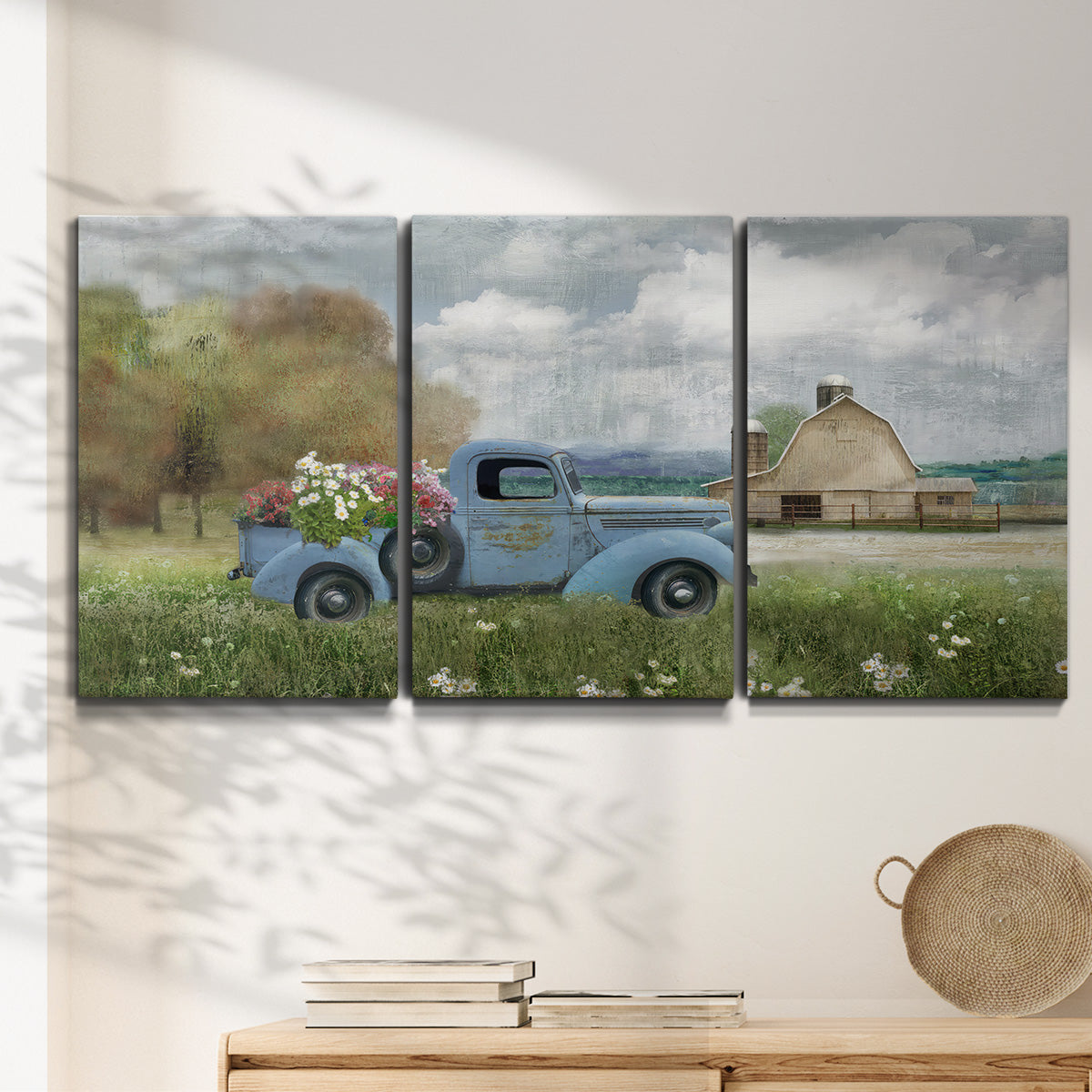 Three-panel canvas wall art featuring vintage blue truck with flower load, displayed in a minimalist living room above a console table.