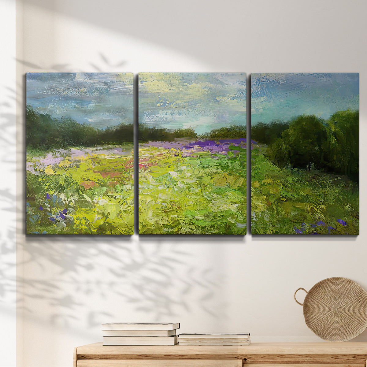 Three-panel canvas wall art featuring pastoral field with wildflowers, displayed in a minimalist living room above a console table.