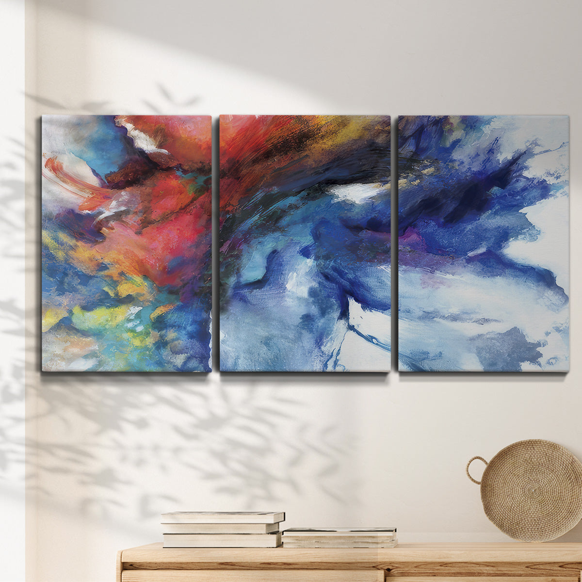 Three-panel canvas wall art featuring vibrant abstract color explosion, displayed in a minimalist living room above a console table.