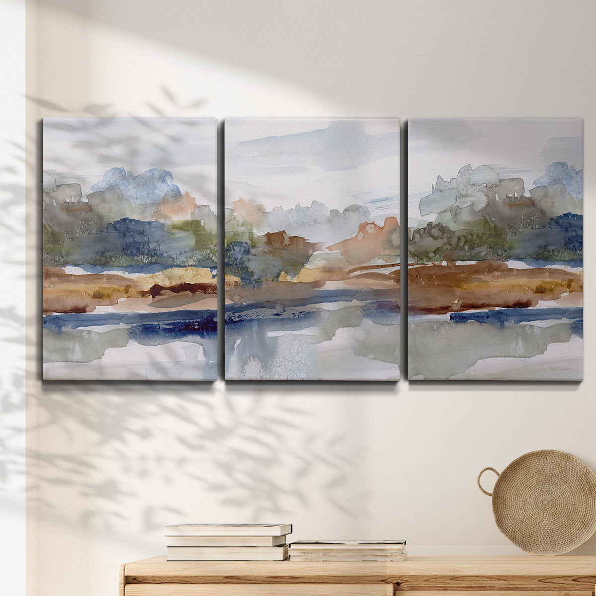 Three-panel canvas wall art featuring layered abstract mountain forms, displayed in a minimalist living room above a console table.