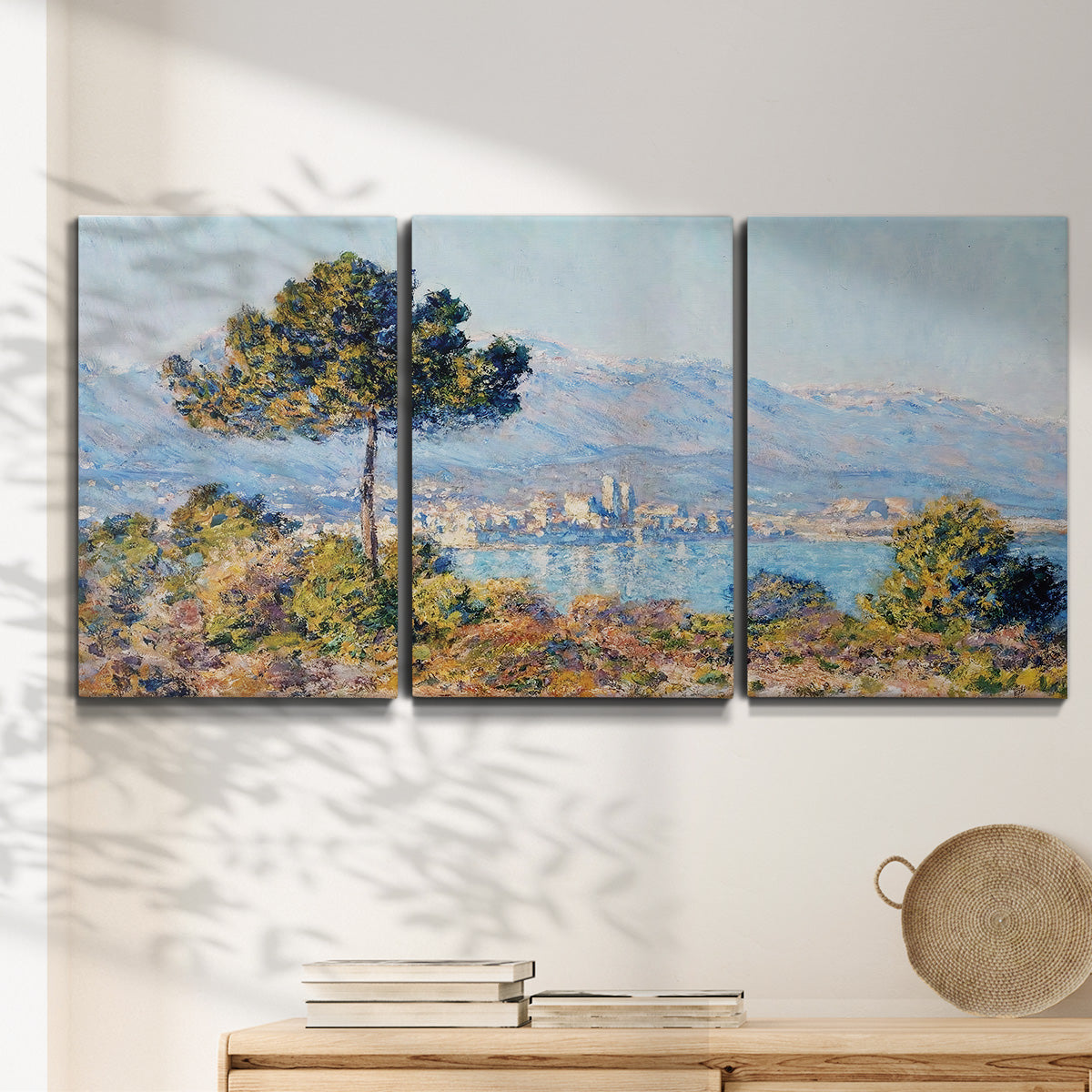 Three-panel canvas wall art featuring coastal town viewed from hillside, displayed in a minimalist living room above a console table.