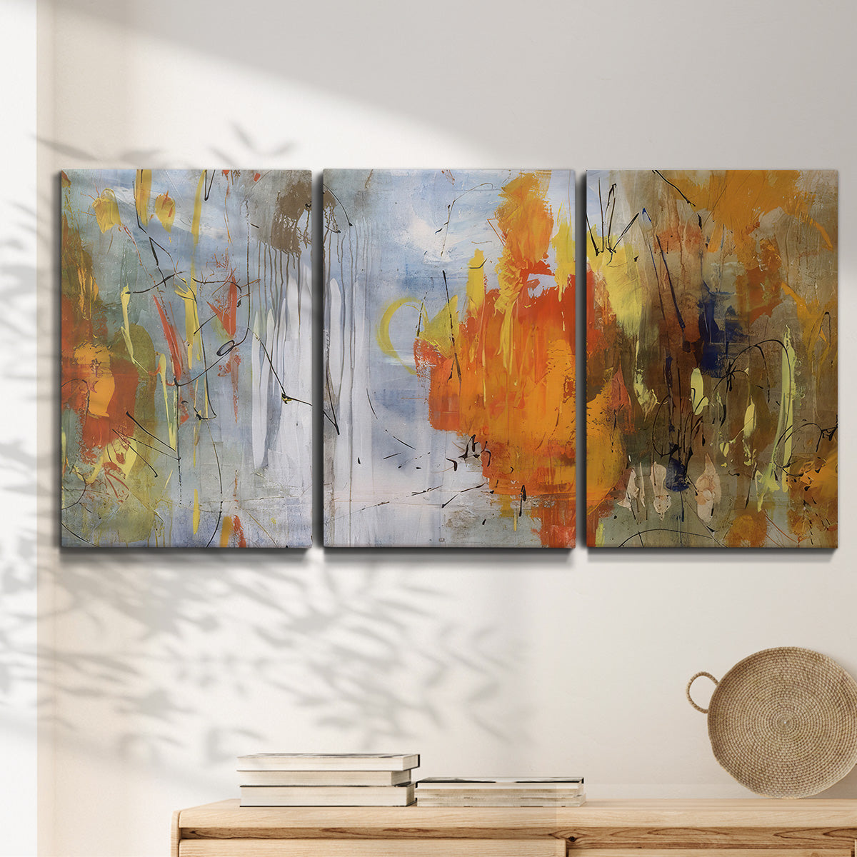 Three-panel canvas wall art featuring abstract warm sunset tones, displayed in a minimalist living room above a console table.