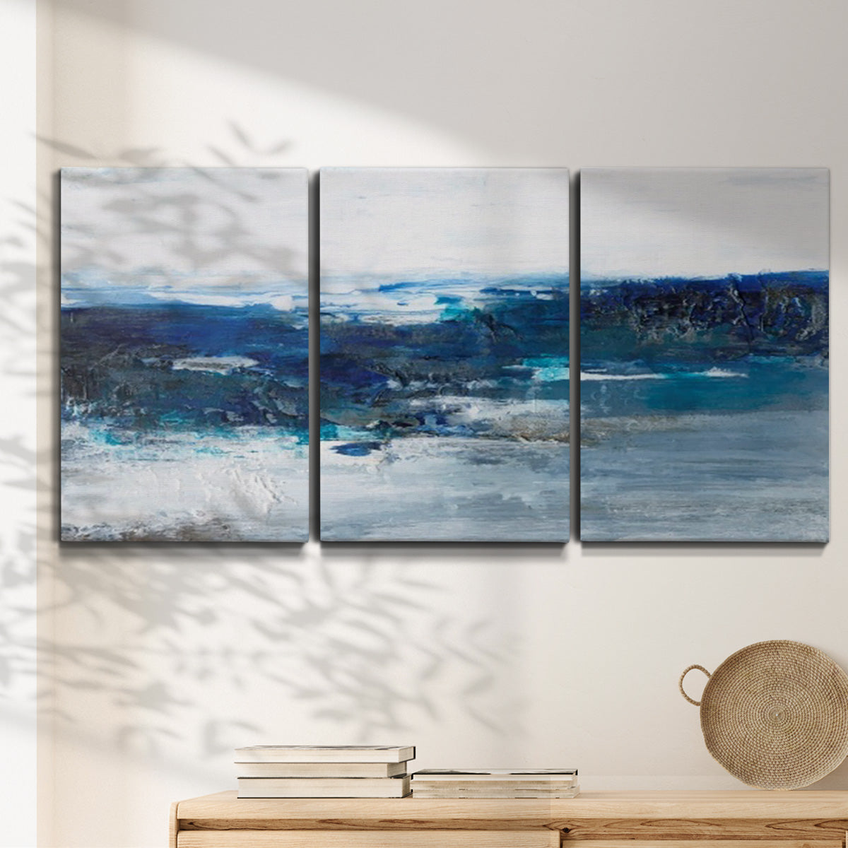 Three-panel canvas wall art featuring moody abstract sea with depth, displayed in a minimalist living room above a console table.