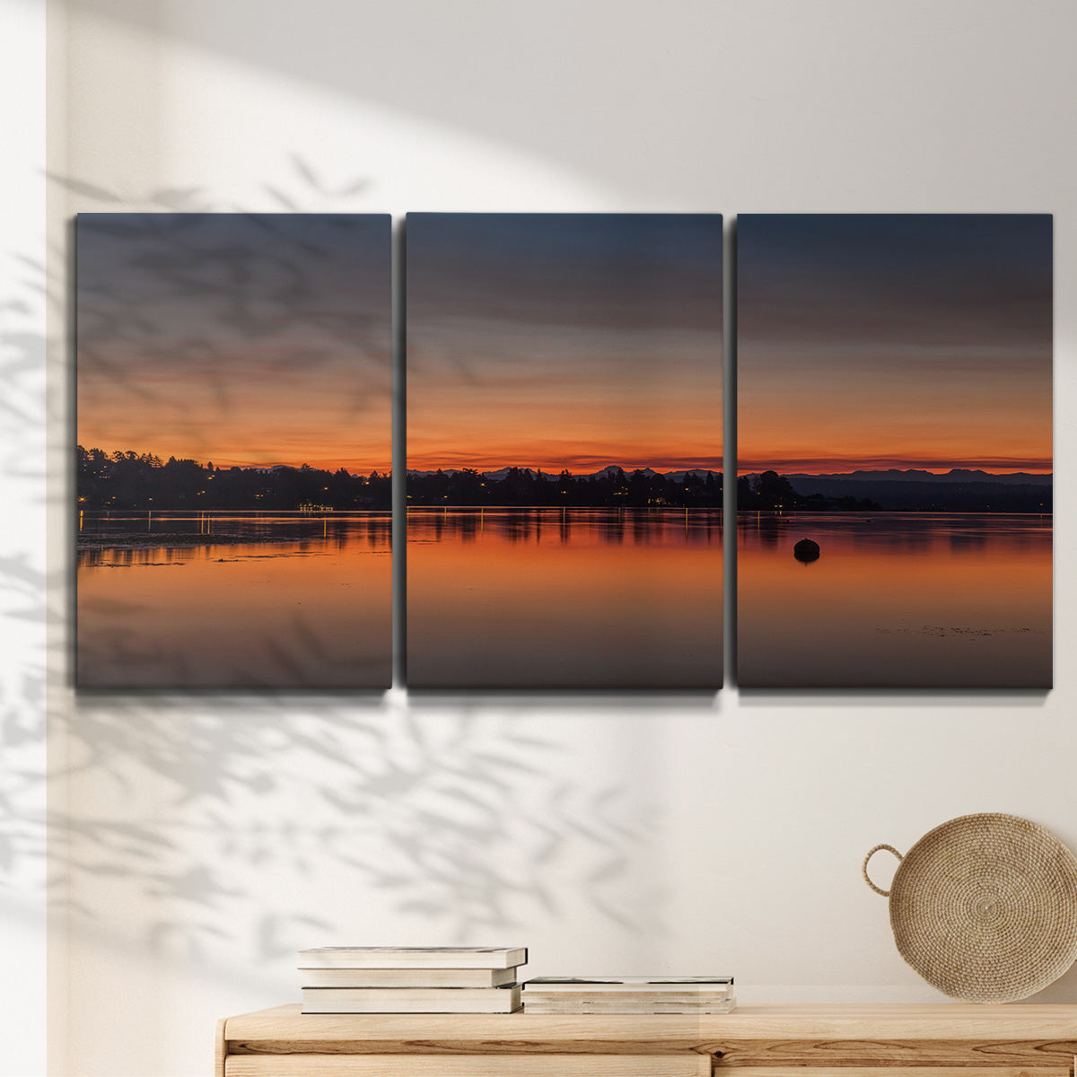 Three-panel canvas wall art featuring glowing sunset over water, displayed in a minimalist living room above a console table.