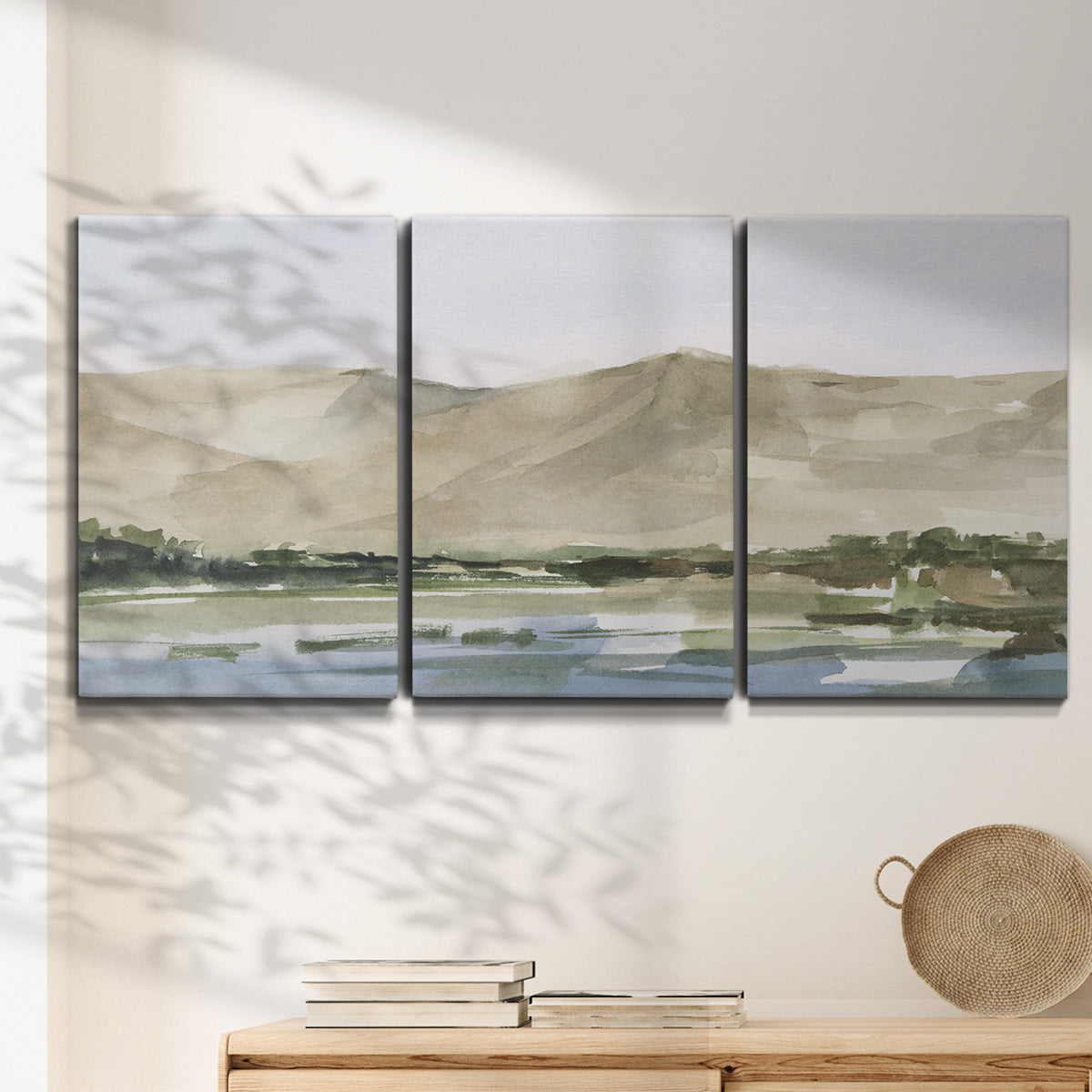Three-panel canvas wall art featuring desert mountain landscape watercolor, displayed in a minimalist living room above a console table.