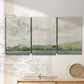 Three-panel canvas wall art featuring riverbank landscape with trees, displayed in a minimalist living room above a console table.