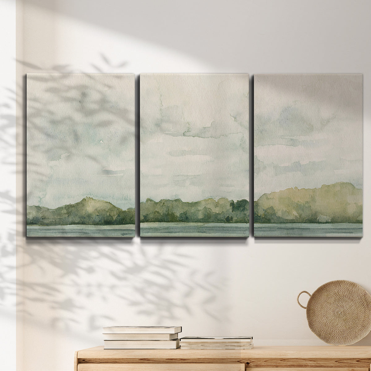 Three-panel canvas wall art featuring riverbank landscape with trees, displayed in a minimalist living room above a console table.