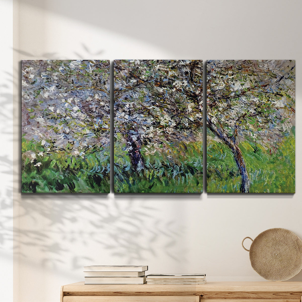 Three-panel canvas wall art featuring apple trees blooming beside water, displayed in a minimalist living room above a console table.