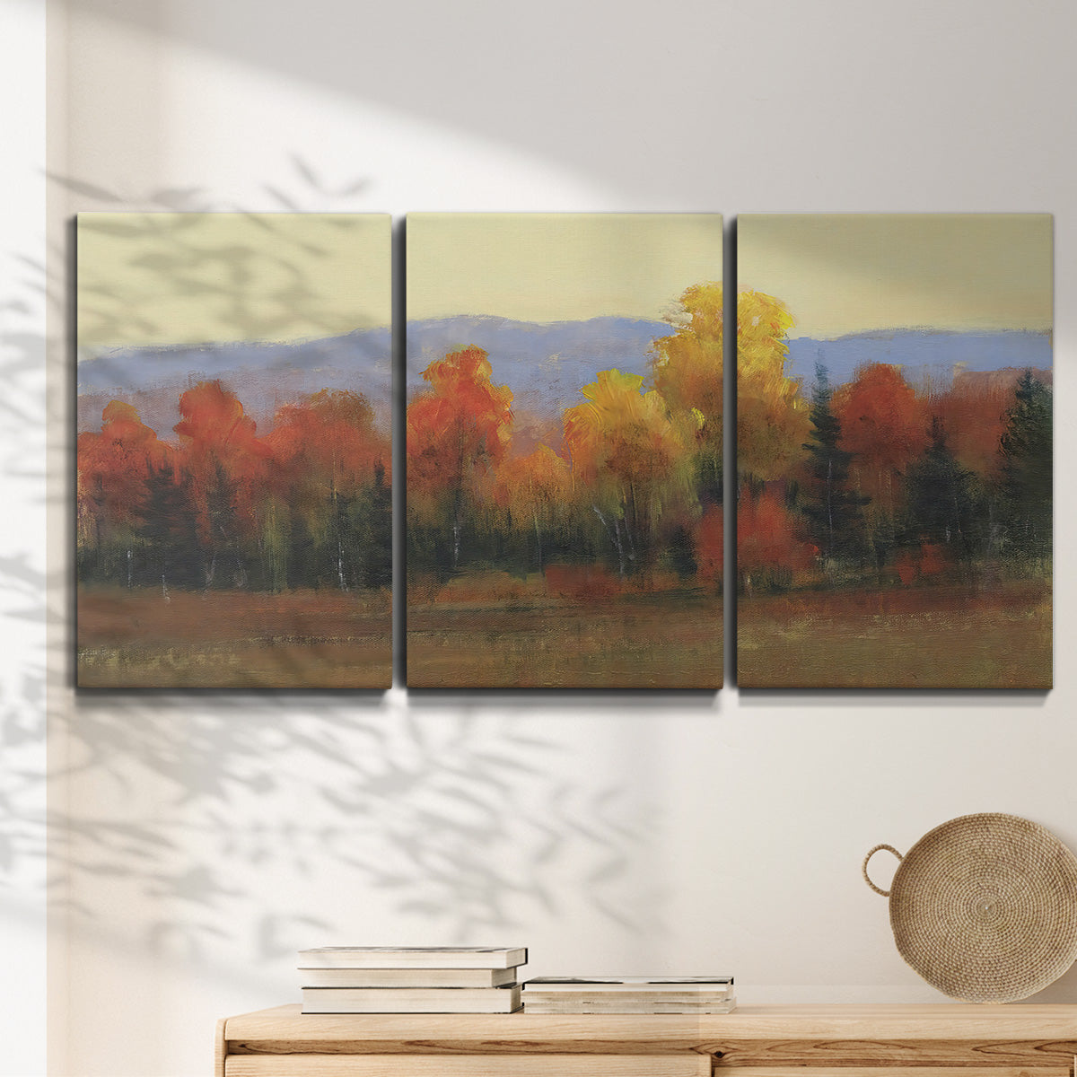 Three-panel canvas wall art featuring autumn landscape changing foliage, displayed in a minimalist living room above a console table.