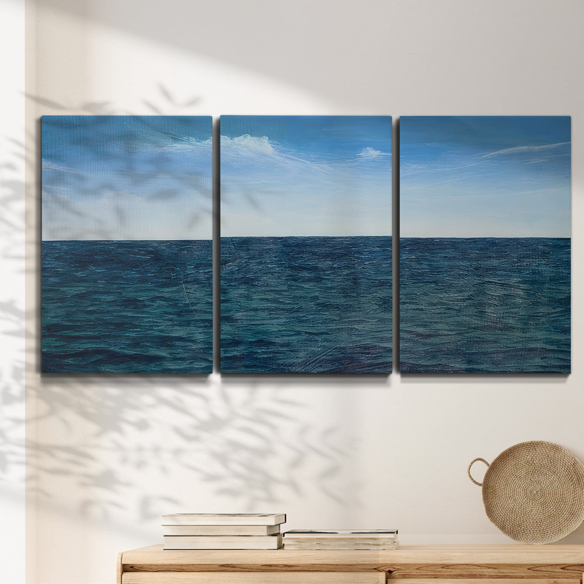 Three-panel canvas wall art featuring open water landscape with wide horizon, displayed in a minimalist living room above a console table.