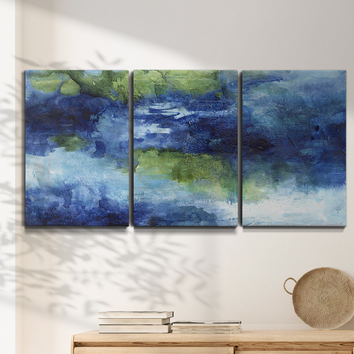 Three-panel canvas wall art featuring flowing blue abstract watercolor, displayed in a minimalist living room above a console table.